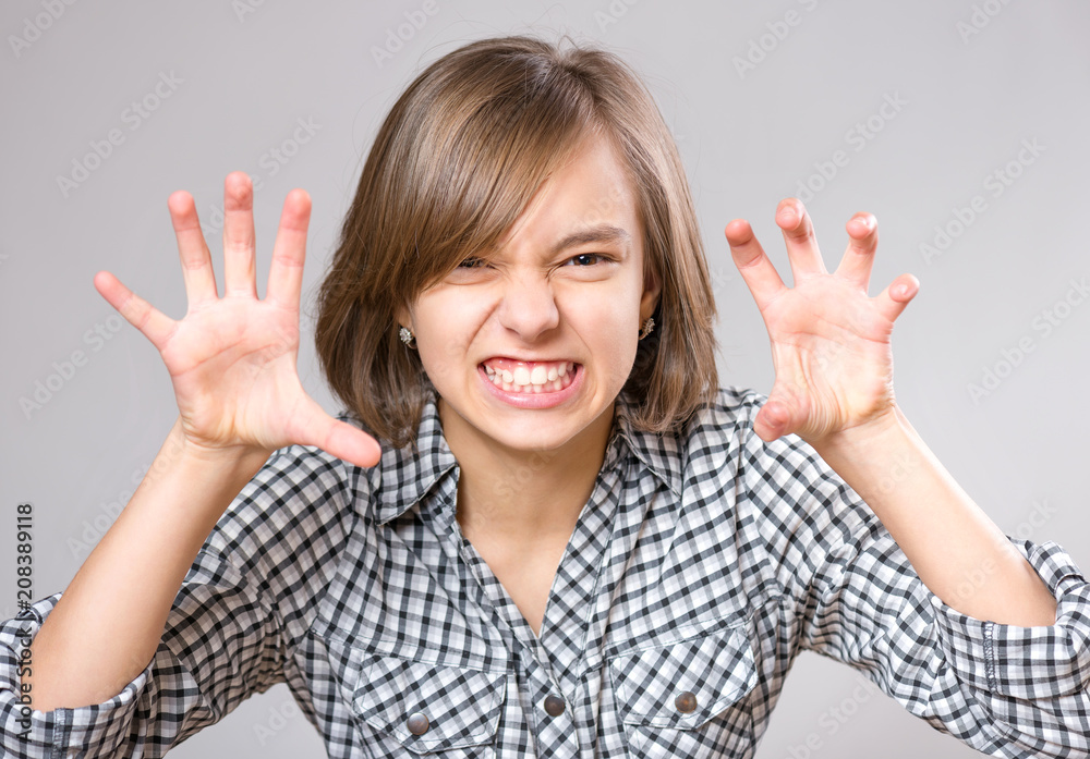 Close-up emotional portrait of attractive angry child teenager girl screaming wide open mouth. Funny cute child on gray background. Negative human face expression. Conflict concept. Close-up emotional portrait of attractive angry child teenager girl screaming wide open mouth. Funny cute child on gray background. Negative human face expression. Conflict concept.