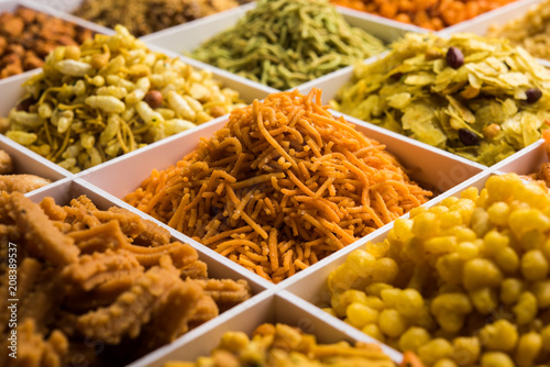 Indian Tea-time snacks like sev, chivda, farsan, mixture, boondi, bakarwadi etc served in white wooden box with cells. selective focus