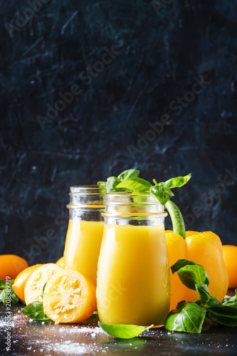 Useful and healthy smoothie or juice from yellow tomatoes and bell peppers with green basil in glass bottles, black background, selective focus
