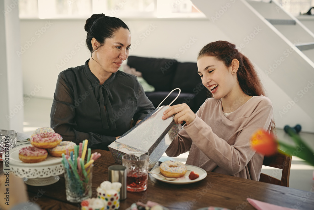 Smiling mother looking at excited daughter with gift during birthday party Smiling mother looking at excited daughter with gift during birthday party