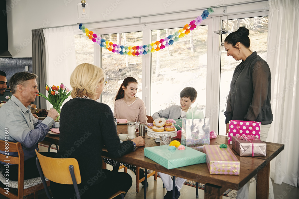 Family looking at boy with gift box while enjoying meal at table during birthday party