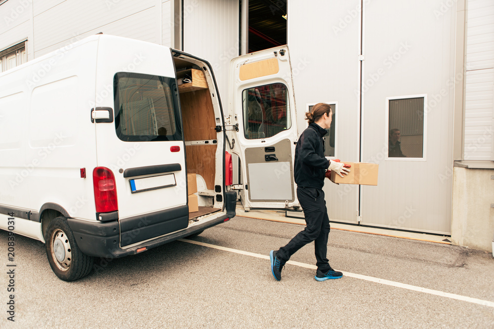 Male worker with box walking against delivery van on road towards entrance Male worker with box walking against delivery van on road towards entrance