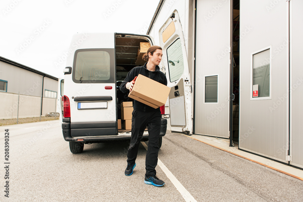 Manual worker carrying cardboard box while walking against delivery van on road Manual worker carrying cardboard box while walking against delivery van on road