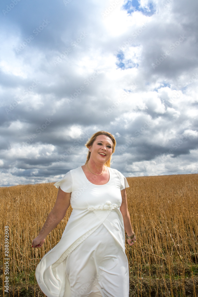 Ausgelassene Frau in weißem Kleid auf Feld vor bewölktem Himmel