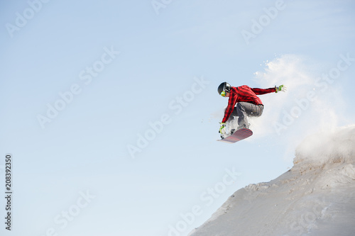 Image of man in helmet with snowboard jumping from snowy mountain slope