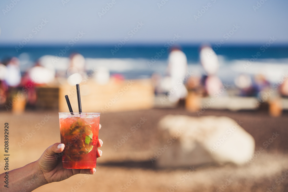Hand are holding strawberry mojito with sunny coast on background.