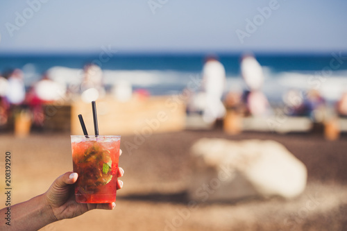 Obraz na płótnie Hand are holding strawberry mojito with sunny coast on background. w salonie