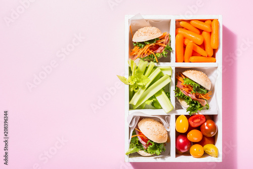Homemade small burgers with ham, tomato, carrot, fresh salad served in old white wooben box on pink background. Healthy junk food concept with copy space. photo