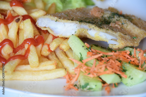 fried fish in breadcrumbs with fries topped with ketchup and a salad of fresh cucumber and grated carrot