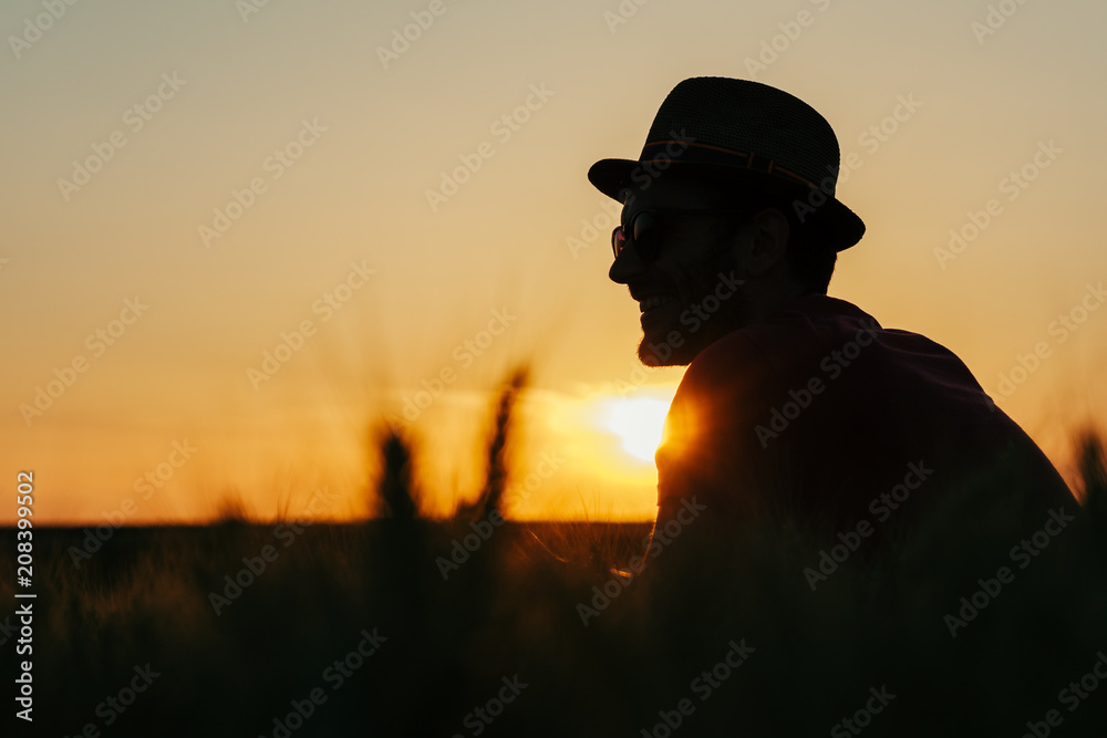 Young man resting in the wheat field at the sunset