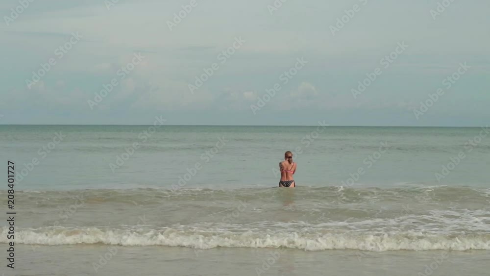 Young women in a bikini in a sea with waves enjoys sunbathing and beach vacation