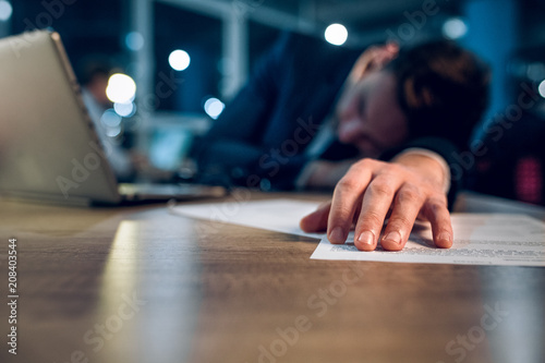 Close up photo of sleeping mans hand on wooden desk. Hand of overworked businessman who stayed up until late night in office working behind laptop. photo