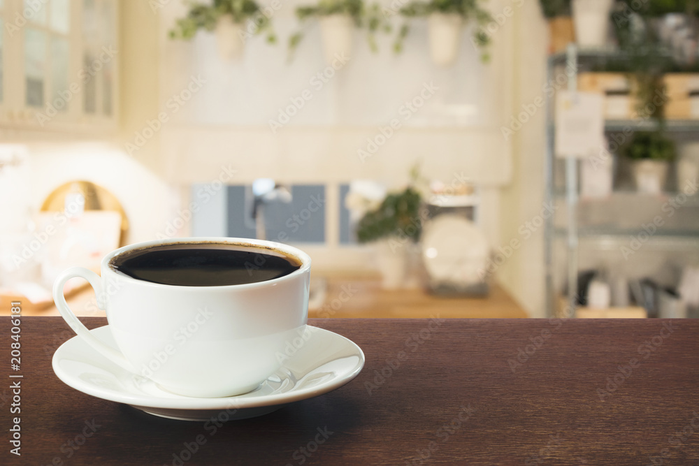 Cup of black coffee on wooden tabletop in blurred modern kitchen. Close up. Indoor.