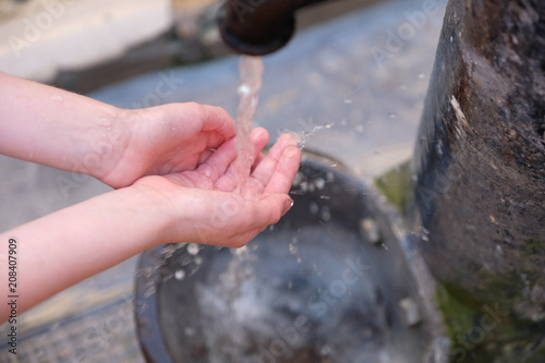 Children's hands under the stream of water from an urban water well