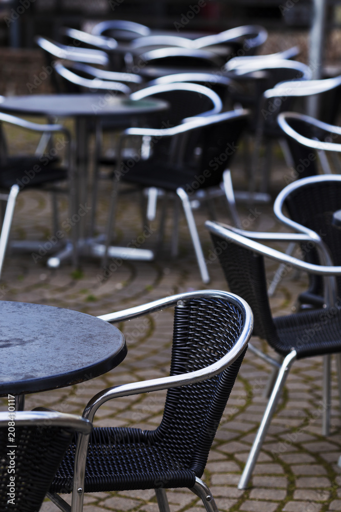 Vacant tables and chairs with shiny metal backrests at street cafe. Selective focus on foreground chair