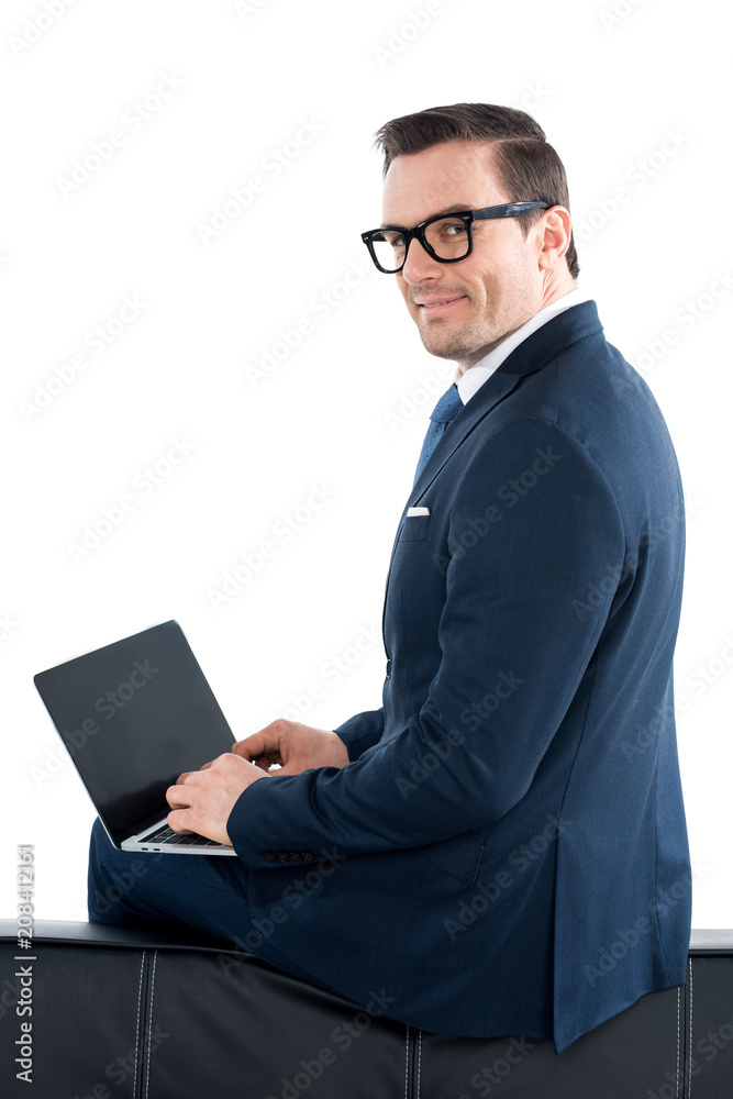 businessman in suit and eyeglasses using laptop with blank screen and looking at camera isolated on white
