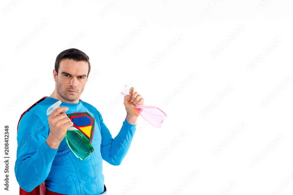 confident superhero holding plastic spray bottles with cleaning liquid and looking at camera isolated on white confident superhero holding plastic spray bottles with cleaning liquid and looking at camera isolated on white