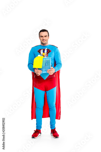 handsome male superhero holding cleaning supplies and smiling at camera isolated on white