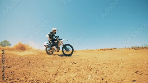 Motorcyclist is driving his bike through dust and sand in slow motion photo