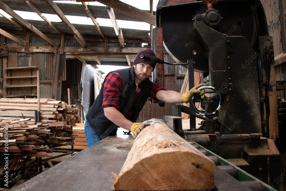 Handsome male lumberjack mills wood with band saw Handsome male lumberjack mills wood with band saw