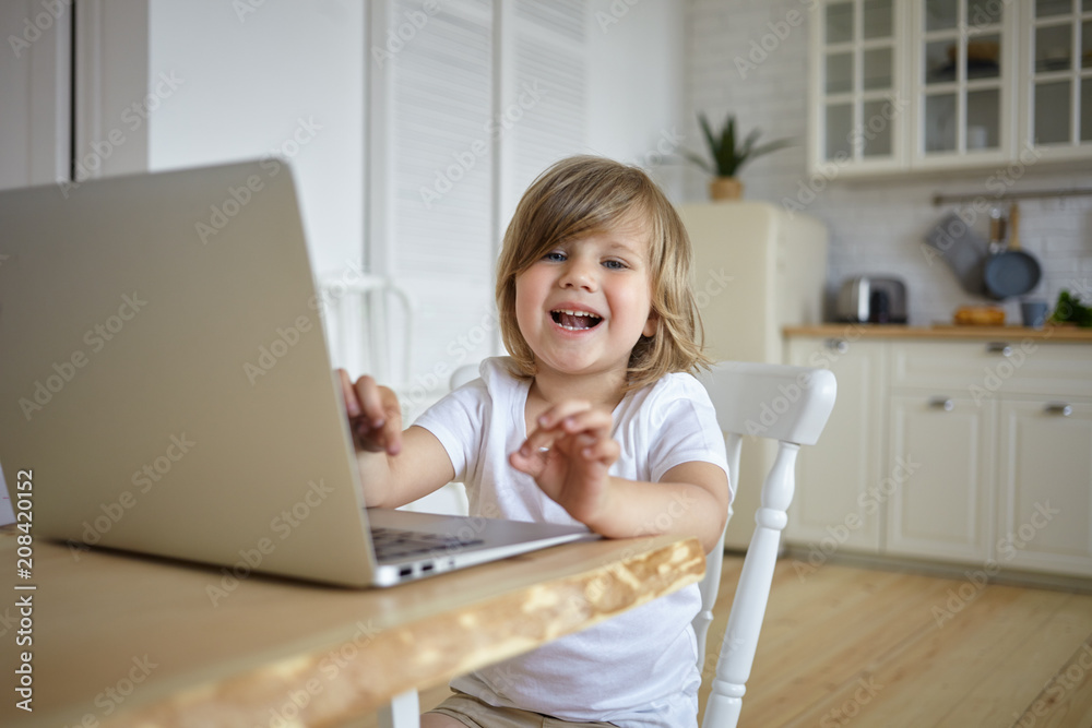 Childhood, modern technology, communication and internet addiction concept. Adorable cute baby girl spending too much time in front of laptop, watching video blog, sitting at table and laughing Childhood, modern technology, communication and internet addiction concept. Adorable cute baby girl spending too much time in front of laptop, watching video blog, sitting at table and laughing