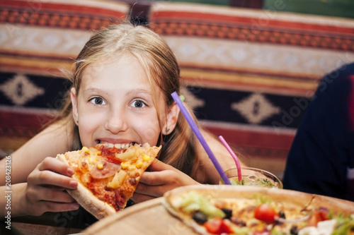 A young girl with great appetite and pleasure eats a delicious pizza at the cafe