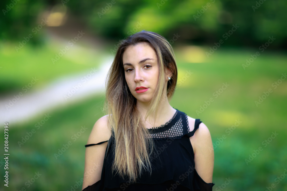 Portrait of a young woman by the park outdoors. A beautiful European girl, of fair complexion, brown hair and brown eyes. 