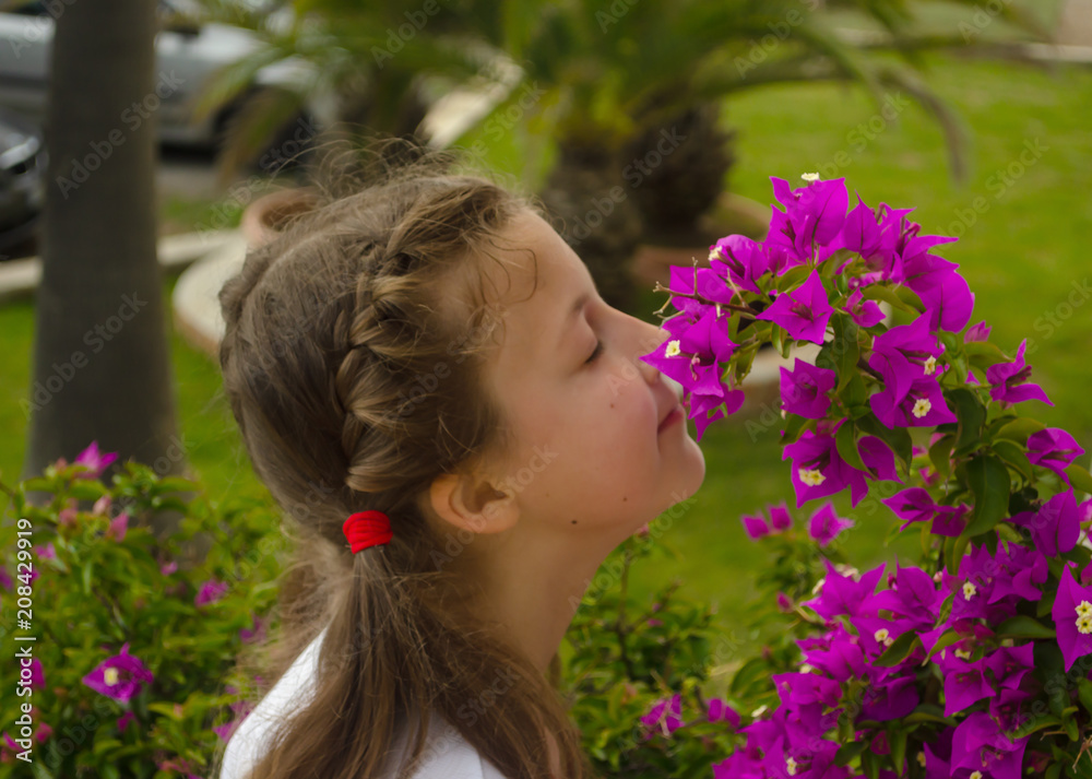Naklejka premium Little adorable girl smelling colorful flowers at summer day