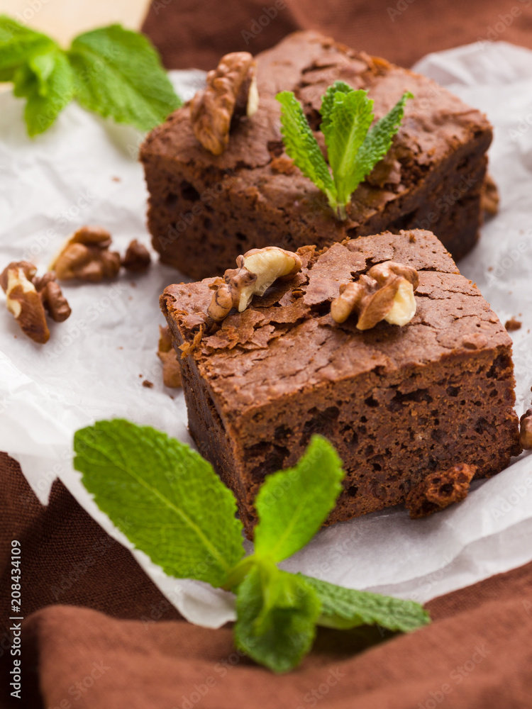 Brownie sweet chocolate dessert with walnuts and meant leaves on white paper with copy space on pastel beige background. Brownie sweet chocolate dessert with walnuts and meant leaves on white paper with copy space on pastel beige background.