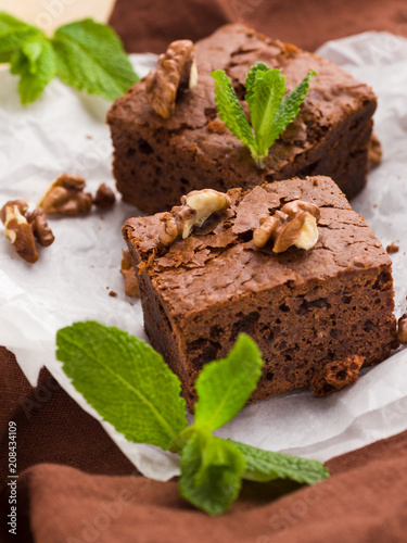 Brownie sweet chocolate dessert with walnuts and meant leaves on white paper with copy space on pastel beige background.