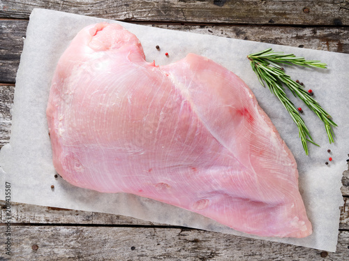 Raw whole big breast turkey fillet with fresh rosmary on a old rustic gray wooden background. Top view. photo