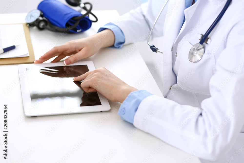 Woman doctor using tablet computer while sitting at the desk in hospital closeup. Cardiologist checks heart diagrams with tablet pc. Healthcare, insurance and smart technology in medicine concept Woman doctor using tablet computer while sitting at the desk in hospital closeup. Cardiologist checks heart diagrams with tablet pc. Healthcare, insurance and smart technology in medicine concept