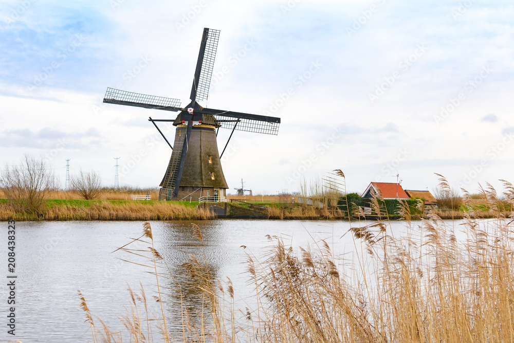 Fototapeta premium Traditional Dutch windmills near the water canals with beautiful white clouds and blue sky reflecting in water. UNESCO world heritage sight in Kinderdijk, Netherlands in winter