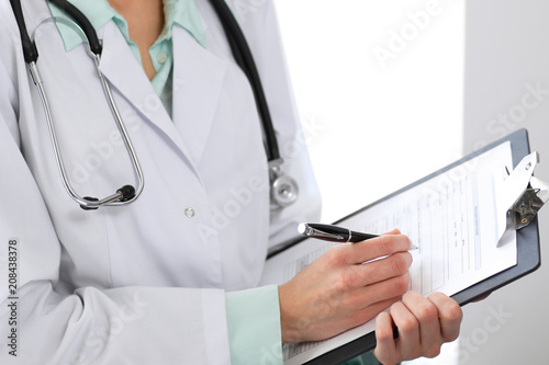 Female doctor filling up medical form on clipboard closeup.  Healthcare, insurance and medicine concept
