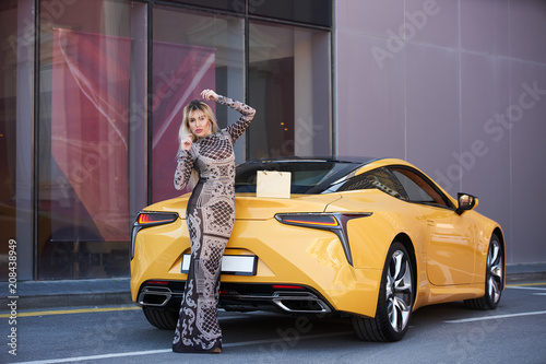 Beautiful blonde young woman with shopping bag near the yellow super car, outdoors © Gecko Studio