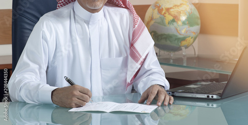 Senior Saudi Businessman Hand Writing At His Desk photo