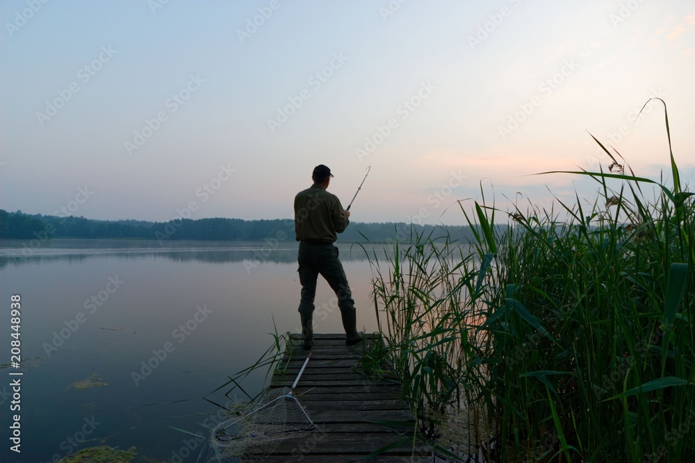 Fisherman catching the fish from wooden pier during dawn