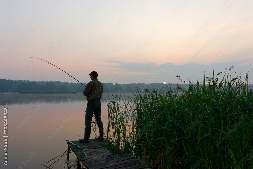 Fisherman catching the fish from wooden pier during dawn