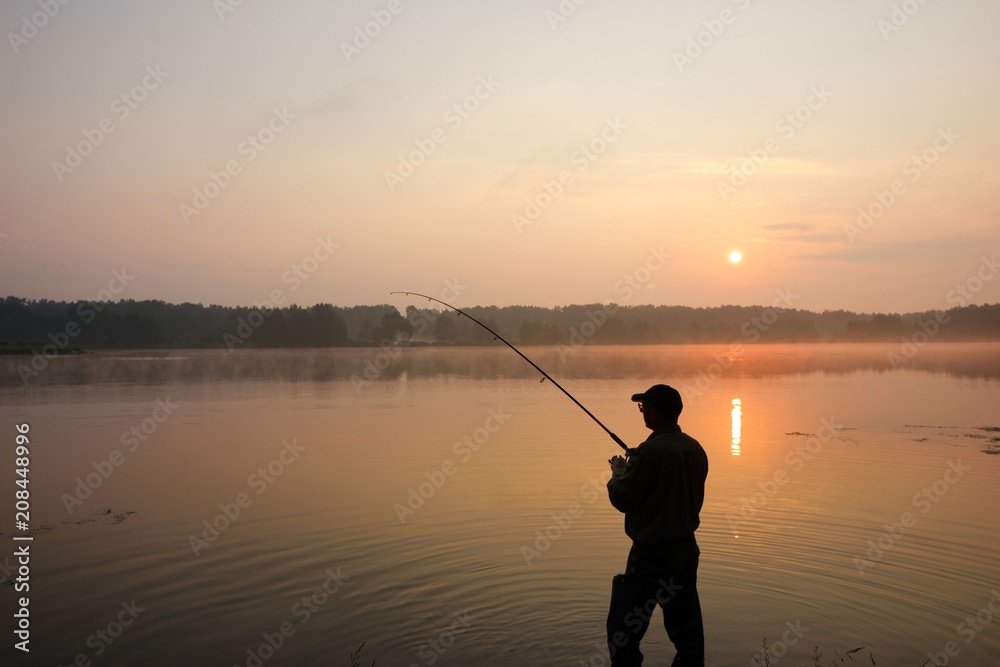 Silhouette of fisherman standing in a lake and catching the fish during sunrise