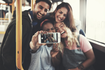 Smiling group of friends taking selfies together on a bus