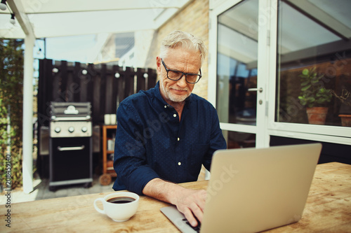 Smiling senior man drinking coffee and using a laptop