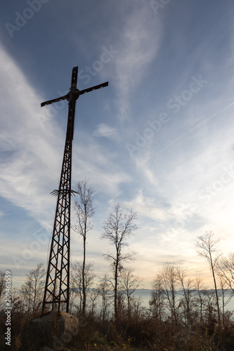 A tall metal crucifix with trees and some fog at golden hour