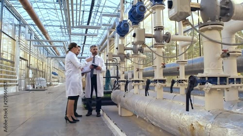Zoom in shot of middle aged woman showing plants and equipment of industrial greenhouse to men in lab coats photo