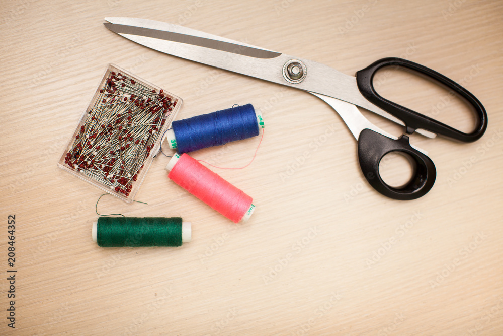 On the cutting table lie scissors, thread and pins. Work place of seamstress. topp view, place for text On the cutting table lie scissors, thread and pins. Work place of seamstress. topp view, place for text