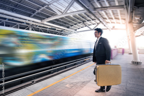 Asian business man walks with his luggage, with motion blur of passing train in the background © chomplearn_2001