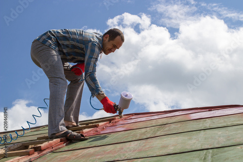 tradesman uses an airless spray to paint the roof