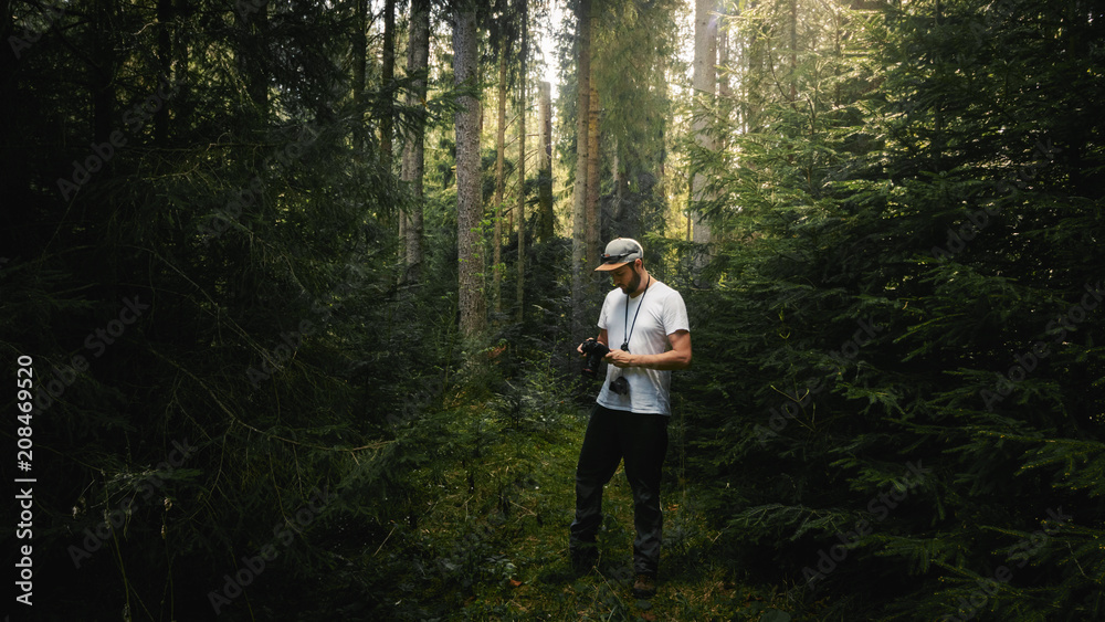 Photographer looking at camera in dark green forest. Light coming from behind Photographer looking at camera in dark green forest. Light coming from behind