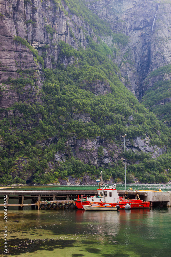 Bright fishing boats anchored to the mooring in the norwegian fjord on the background of the steep cliff, Norway