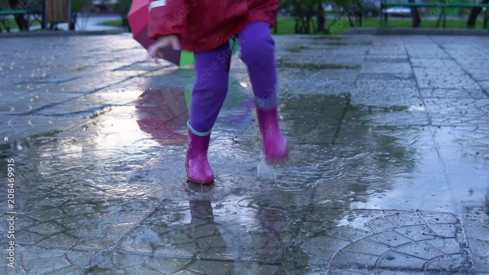 A cute little girl in a red raincoat jumping over a puddle in the park at sunset. The child smiles and enjoys the fun. A cute little girl in a red raincoat jumping over a puddle in the park at sunset. The child smiles and enjoys the fun.