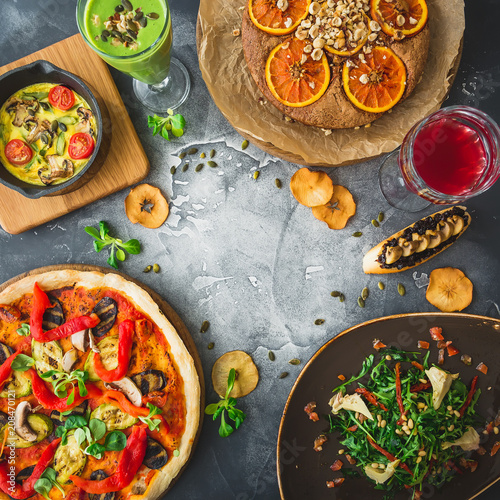 Vegetarian food - pizza with vegetables, salad, pie and fruit drinks on dark background. Flat lay, top view. Food background